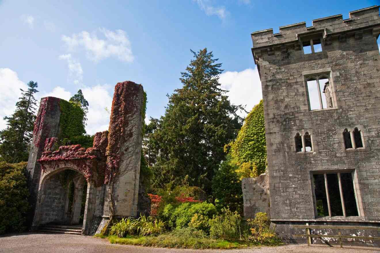 Old stone building ruins surrounded by lush greenery and blue sky. One structure has ivy growing over it, while the other has multiple windows and a battlement.