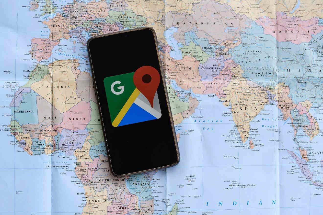 A smartphone displaying the Google Maps app icon rests on an unfolded world map.