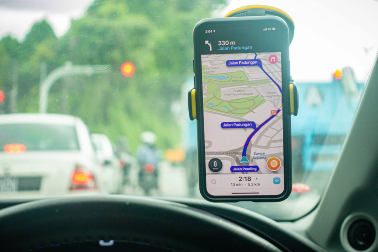 A smartphone mounted on a car dashboard displays a navigation app directing to 