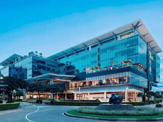Glass facade of AC Hotel by Marriott San José Escazú in Costa Rica at dusk, with landscaped grounds and a lit ground-floor restaurant.