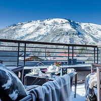 A rooftop terrace with a table set for breakfast, overlooking snow-covered mountains under a clear blue sky.