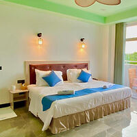 A hotel room with a neatly made bed adorned with blue and white bedding, two bedside tables with lamps, and a sliding door leading to a balcony.