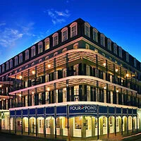 A four-story building with balconies on each level, labeled "Four Points by Sheraton," lit up against a deep blue evening sky.