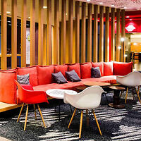A modern lounge area with a red sofa, gray cushions, white and red chairs, wooden partition, and colorful lighting.