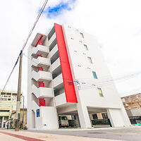 A modern white six-story apartment building with red accents and an external staircase, situated on a city street with power lines overhead.