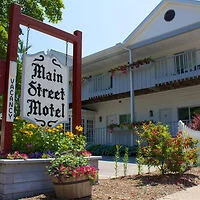 Exterior of Main Street Motel with a prominent sign, potted plants, flowers, greenery, and a balcony.
