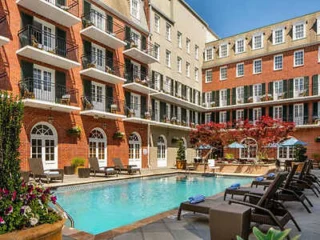 Outdoor courtyard with a swimming pool, surrounded by lounge chairs and a red-brick, multi-story building with numerous balconies.