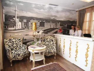A cozy hotel lobby with a classic black-and-white photograph mural, ornate chairs, and a white reception desk with gold accents.