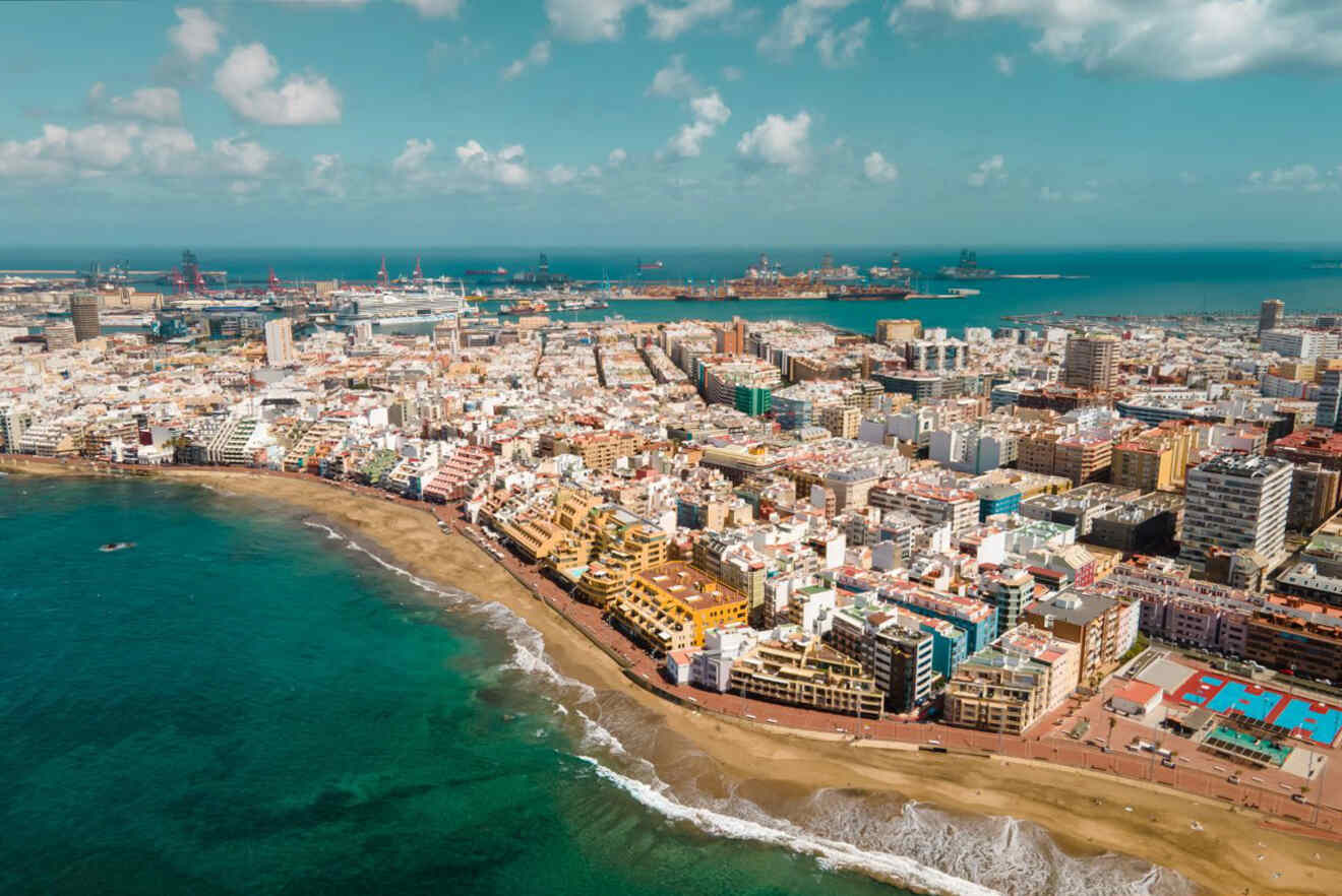 Aerial view of a coastal city with numerous buildings near a beach and blue ocean under a partly cloudy sky.