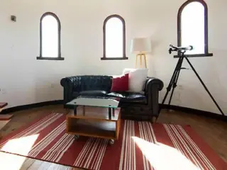 A unique living space with a leather sofa, telescope, and distinctive arched windows providing natural light