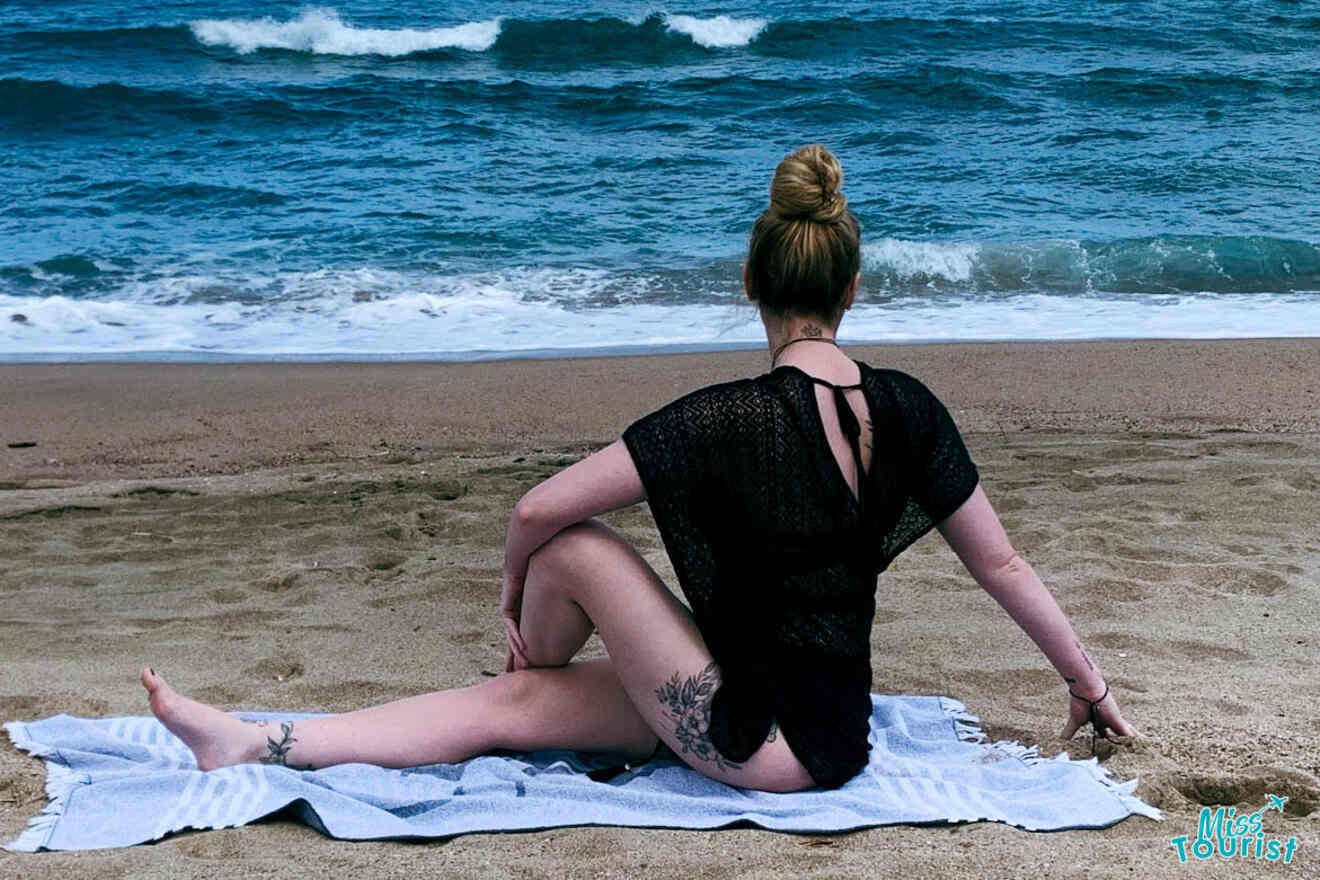 The writer of the post doing a seated twist pose on the beach, facing the ocean waves.