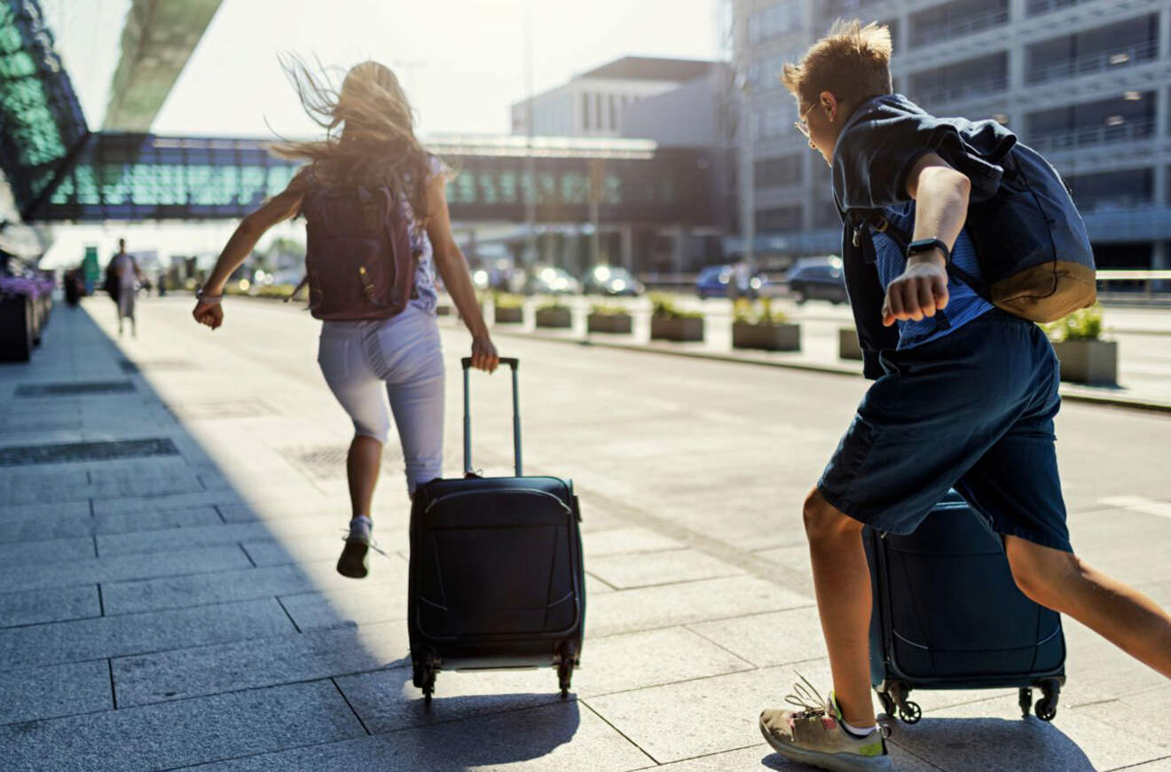 Two people running with their suitcases outside an airport, suggesting a rush to catch a flight