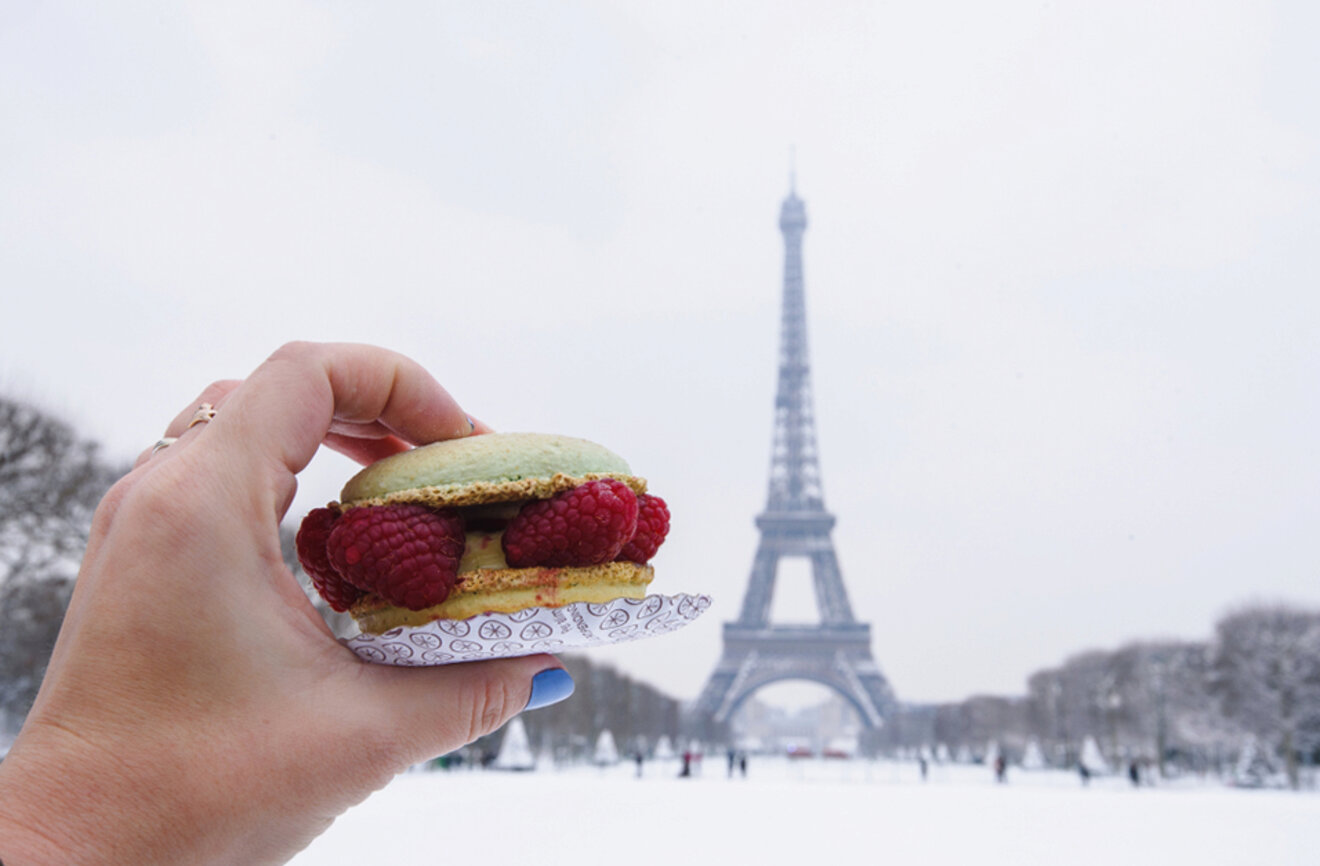 Hand holding a green macaron with raspberries, with the Eiffel Tower in the background in Paris, France.