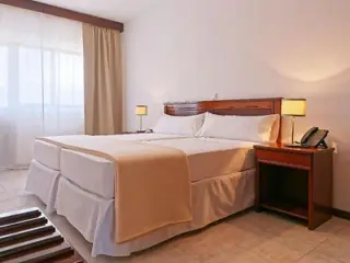 A bright, minimalist bedroom with two single beds pushed together, dressed in white linens, and wooden accents