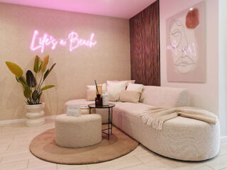 A chic and cozy living area with a white sofa, stylish decor, and a neon sign reading "Life's a Beach."