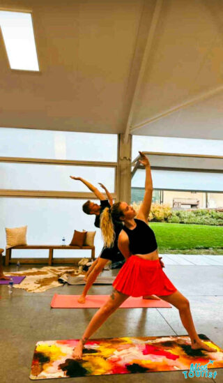 The writer of the post and a group of people practicing yoga in a studio, with the writer doing a side angle pose in a red skirt.