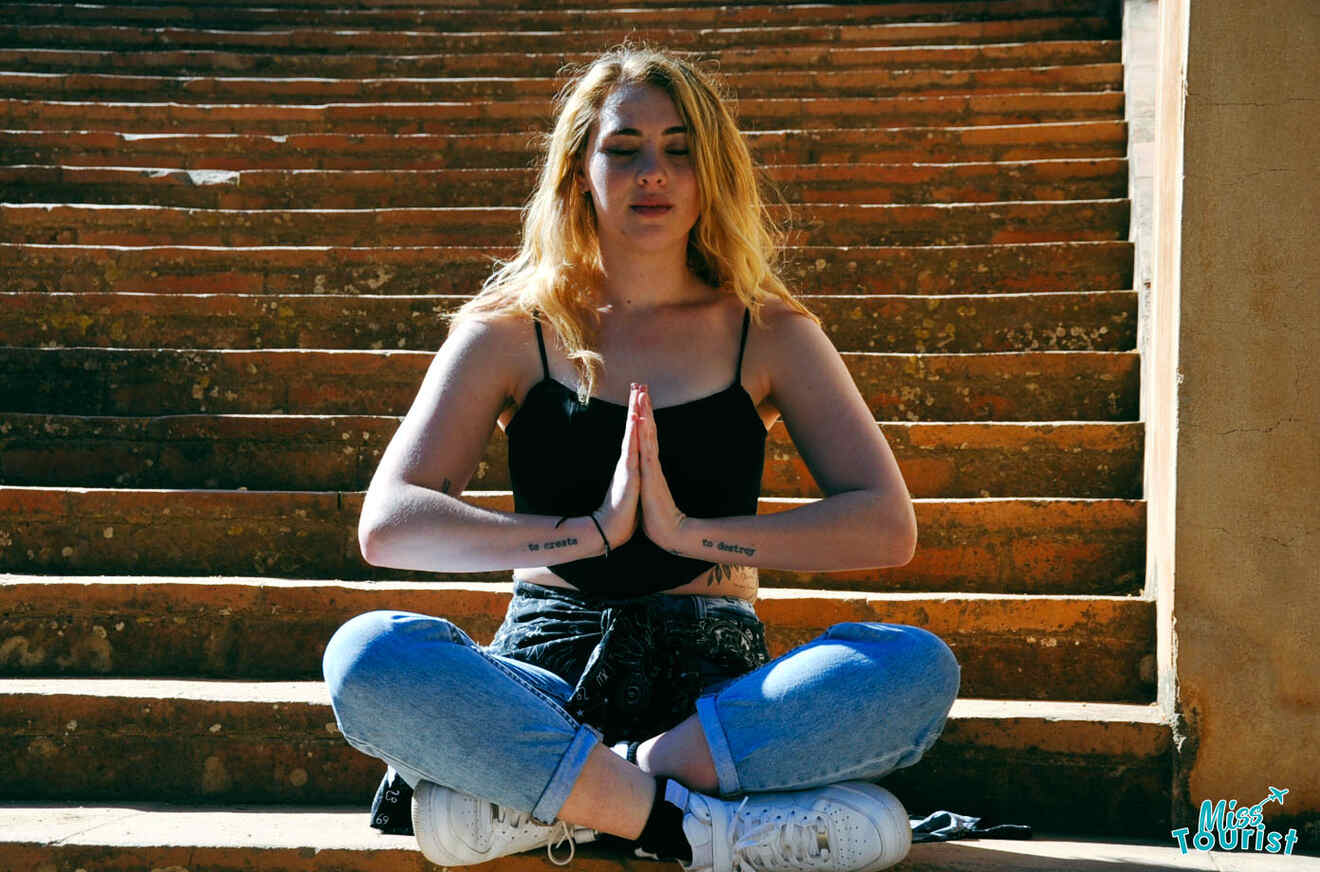 The writer of the post sitting in a meditative pose on stone steps, with hands in a prayer position and eyes closed.