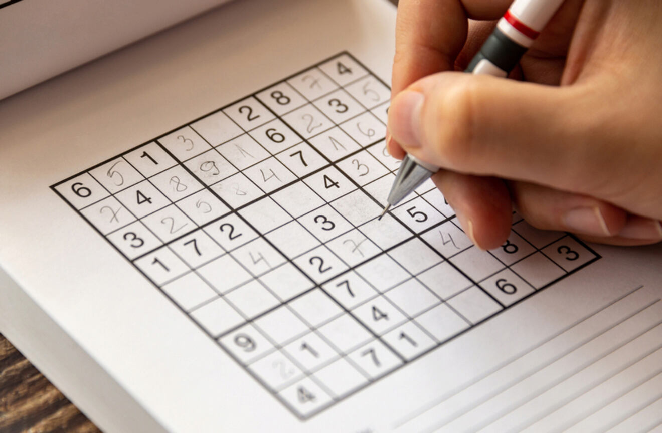 A close-up of a person solving a Sudoku puzzle with a pen.