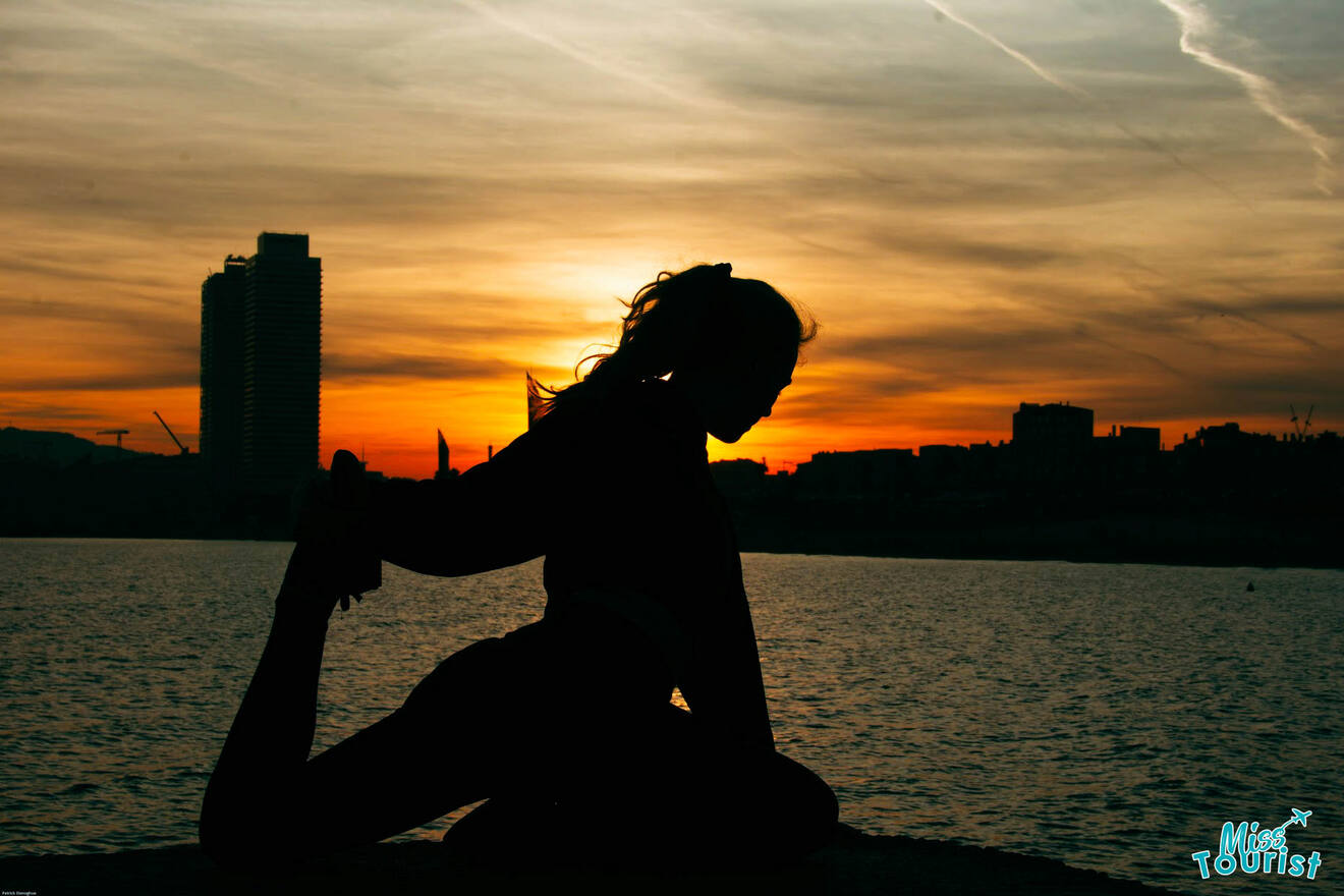 The writer of the post silhouetted against a sunset, doing a yoga stretch by the water with city buildings in the background.