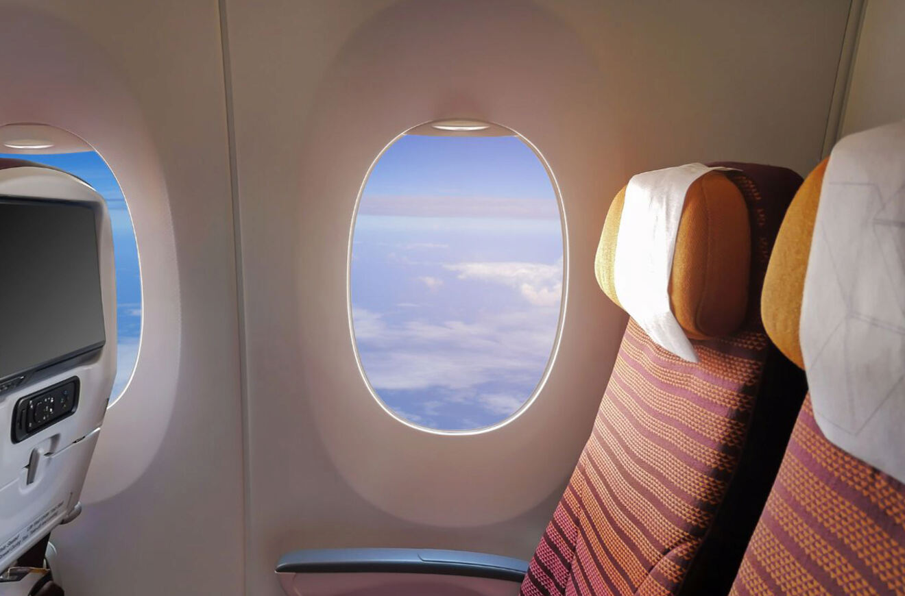 A pair of empty airplane seats with a window view of the sky and clouds.