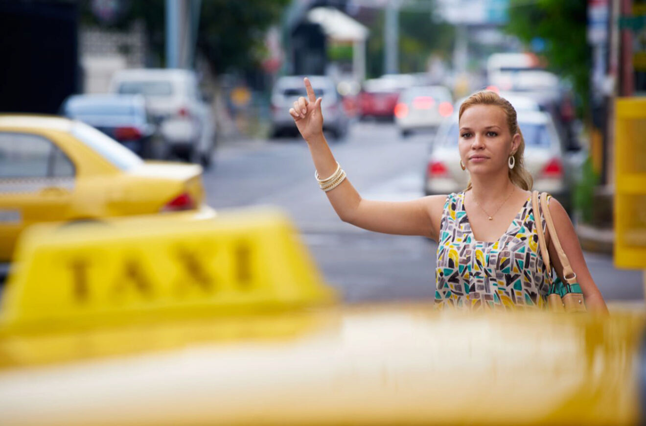 Woman hailing a taxi on a busy city street, with a yellow taxi in the foreground