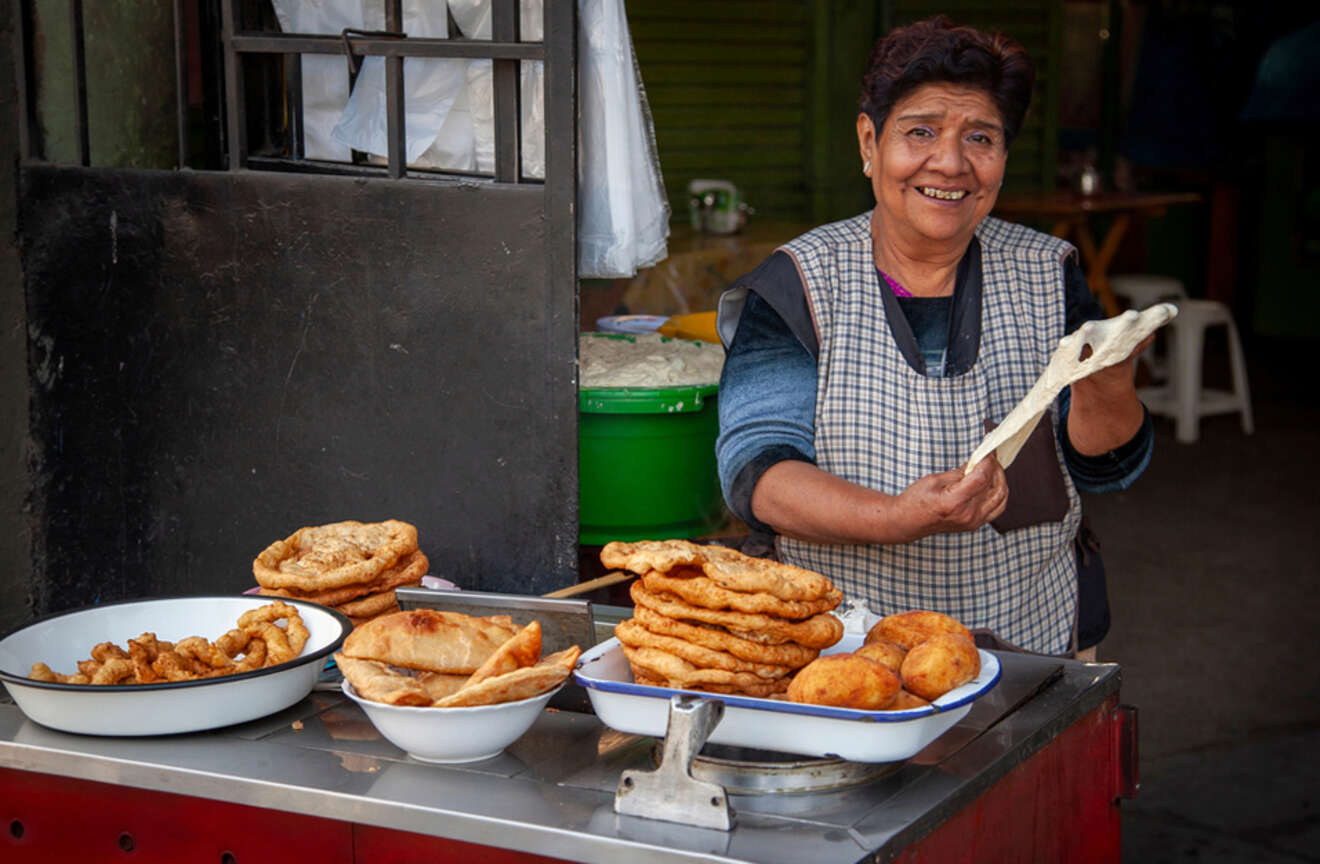 Smiling woman at a street food stall displaying various fried pastries in Lima, Peru.