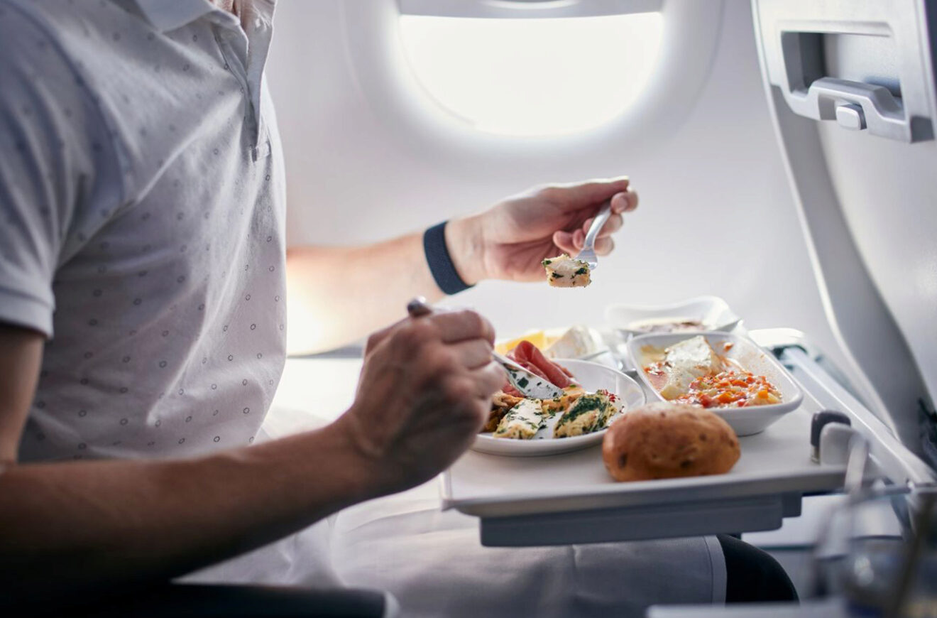 A man eating a meal from a tray table on an airplane, with various dishes in small containers.