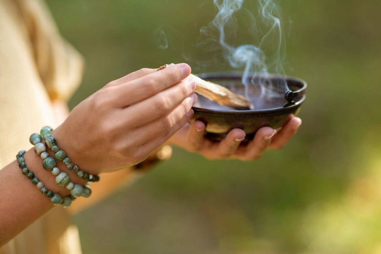 A person's hand holding a smoking bowl while wearing green beaded bracelets on the wrist.