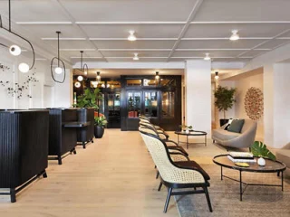 Modern hotel's lobby with a reception desk on the left, seating area with chairs and tables in the center, and decorative lighting and plants.