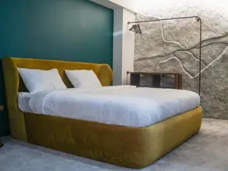 A stylish bedroom with a unique, contemporary design featuring a green accent wall, a large bed with a golden headboard, and an artistic light fixture.