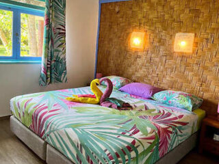 A cozy bedroom with tropical-themed bedding, a thatched accent wall, and colorful towel art.