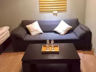 A comfortable living room setup with a dark gray sofa, two white pillows, a black coffee table, and a tray with bottled water.