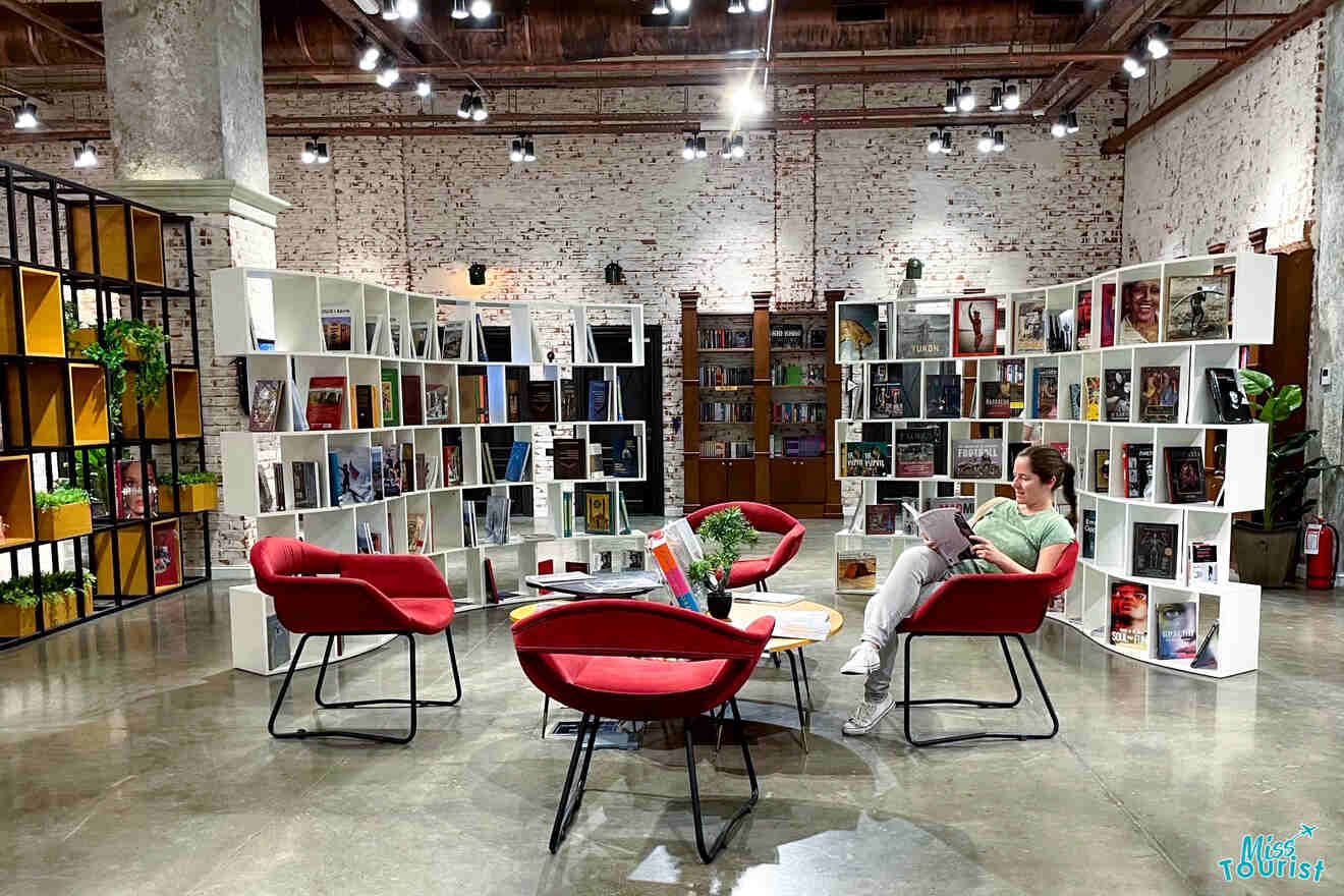 author of the post read a book while sitting on a red chair in a well-lit library with modern furniture and white shelving units filled with books.