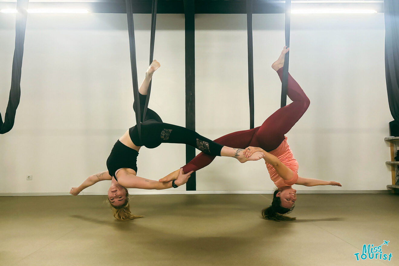 The writer of the post performing acrobatic yoga poses using aerial silk hammocks, holding a partner's legs while upside down.