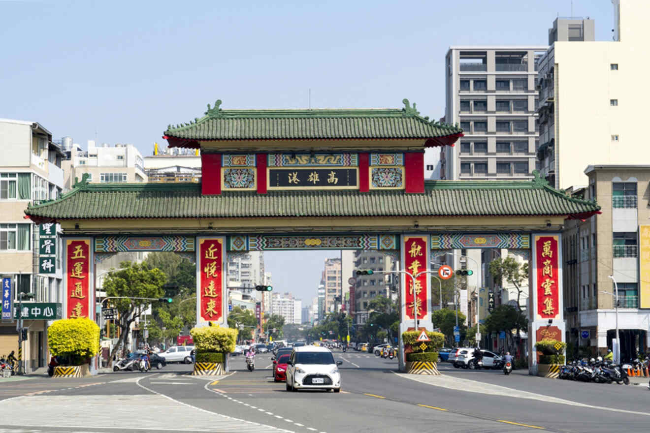 A traditional Chinese archway adorned with red and gold decorations spans a busy urban street with cars and buildings in the background.