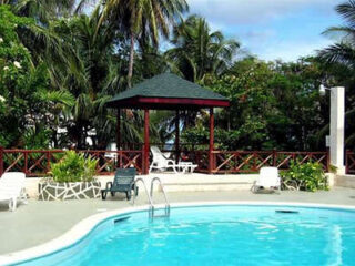 Outdoor swimming pool with lounge chairs and a gazebo surrounded by palm trees.