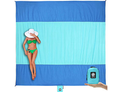 Woman in a green bikini lies on a blue beach blanket with a wide-brimmed hat covering her face. A compact, folded version of the blanket is shown in the lower right corner.