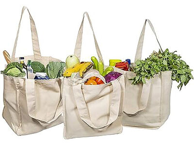 Three reusable canvas bags filled with groceries, including bananas, lettuce, carrots, and leafy greens.