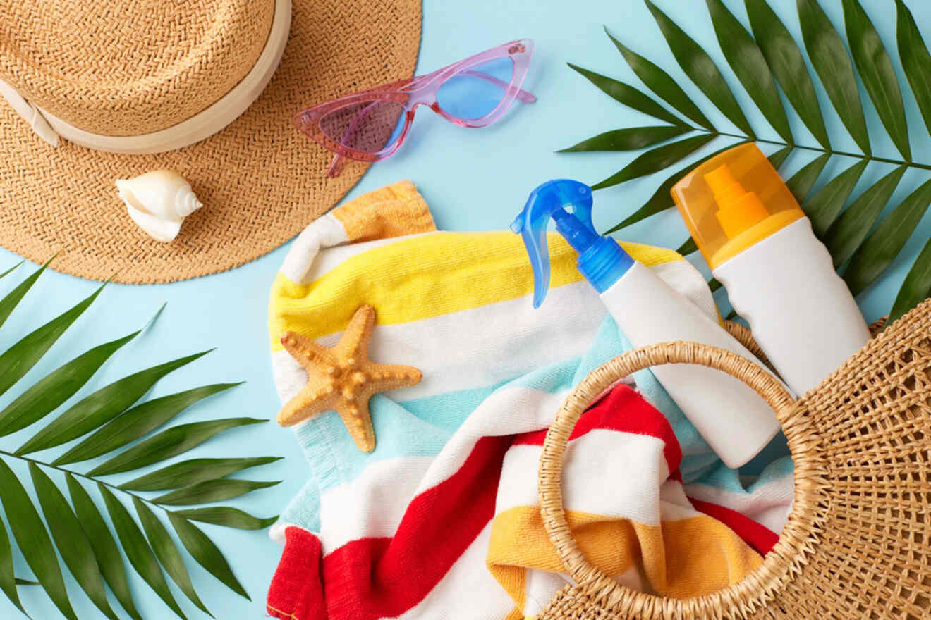 Beach items including a straw hat, sunglasses, sunscreen, a starfish, seashell, and a colorful striped towel are arranged on a light blue background with palm leaves.