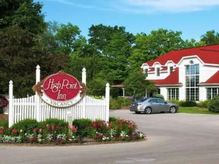 Outdoor view of High Point Inn featuring a white picket fence, red sign with "Vacancy," manicured landscaping, and a building with red roof and dormer windows.