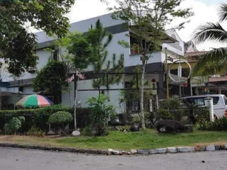 A two-story house with a garden, trees, and shrubs in front. There is a white van parked by the side of the house and a multicolored umbrella near the entrance.