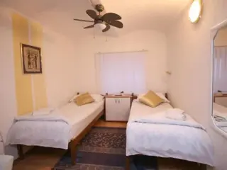 A cozy bedroom with two single beds, a small central cabinet, and a ceiling fan, offering a simple yet comfortable stay.