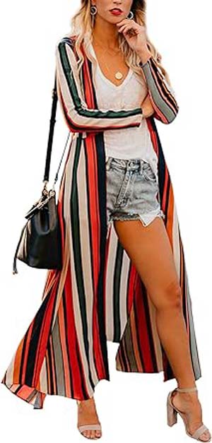 Person wearing a long, colorful striped cardigan over a white top and denim shorts, with a black shoulder bag and beige high-heeled shoes.
