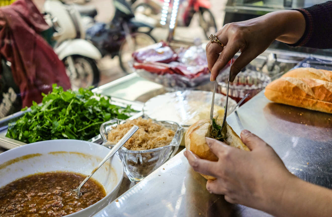 Close-up of hands preparing a banh mi sandwich at a street food stall in Ho Chi Minh City, Vietnam.