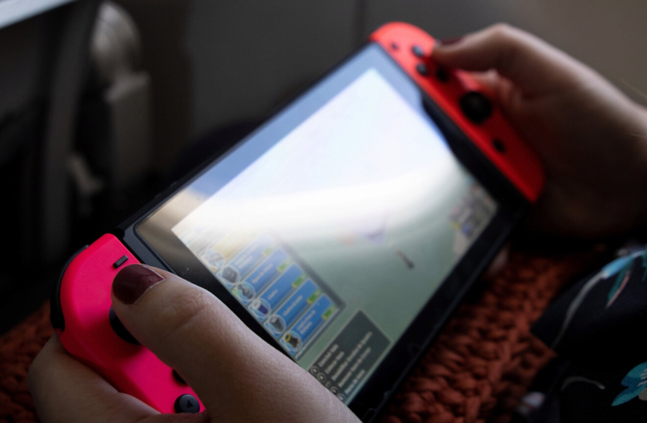 Close-up of hands holding a gaming console with red controllers, displaying a game screen.