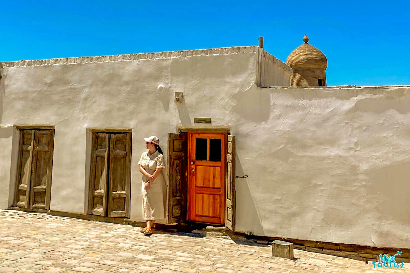 author of the post in white stands outside a white building with wooden doors under a clear blue sky. Dome visible in the background.