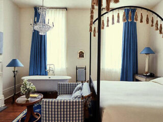 A bedroom with a canopy bed, clawfoot bathtub, chandelier, blue and white checkered furniture, and blue curtains.