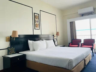 A hotel room with a neatly made bed, two bedside tables, wall-mounted lamps, two chairs near a window with curtains, and framed art on the wall.