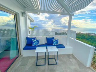 A modern outdoor seating area with blue cushions, white furniture, and a scenic view of the ocean.