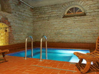 An indoor pool set in a rustic brick-walled room with vintage wooden loungers.